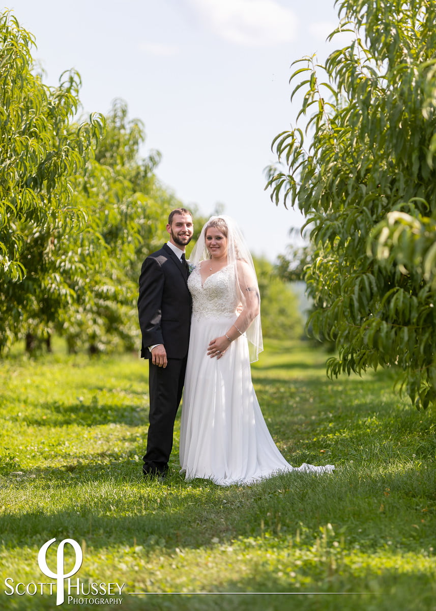 A country bride and groom standing in a peach orchard.