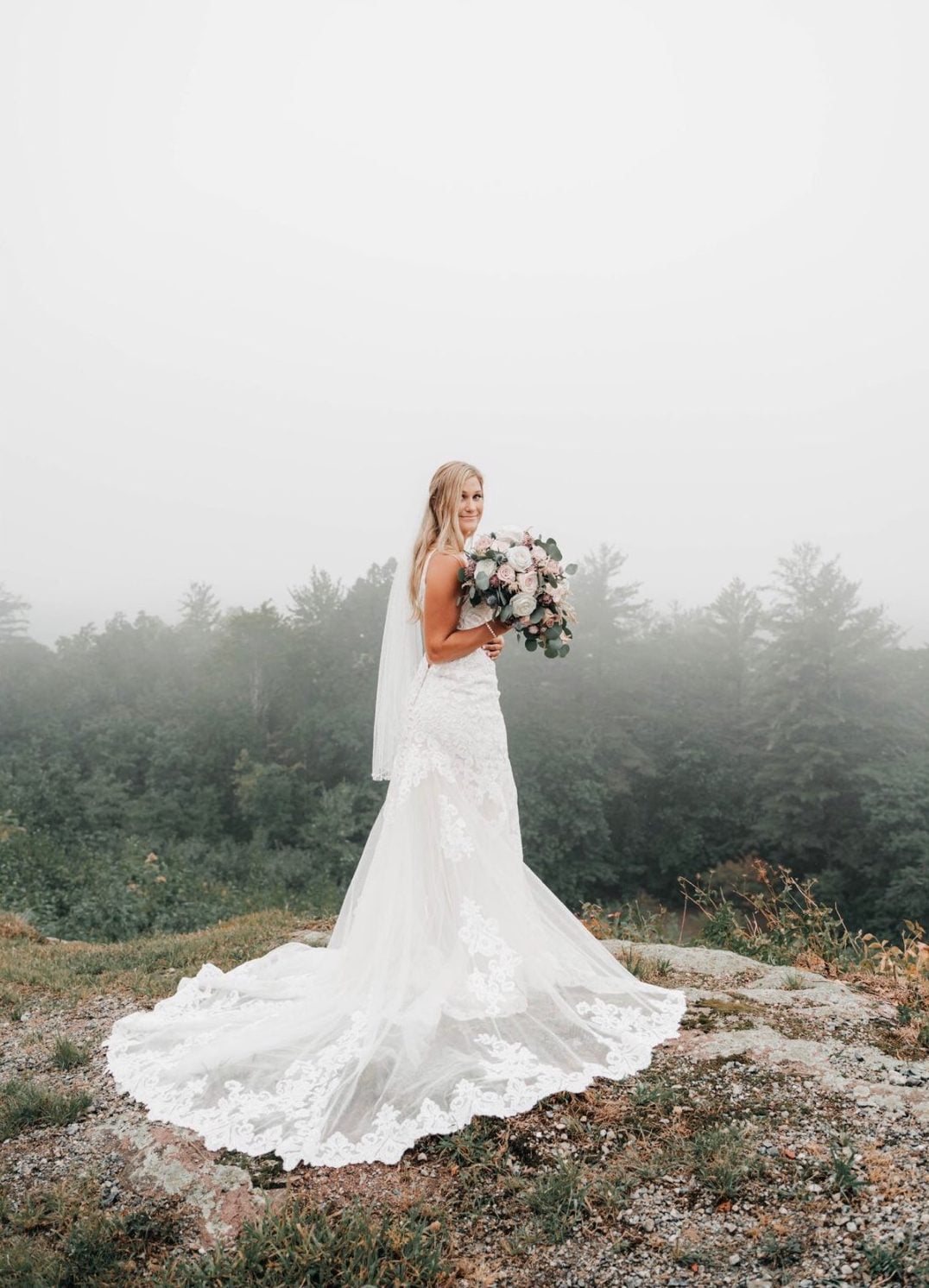 A country bride standing on top of a mountain in a foggy day.