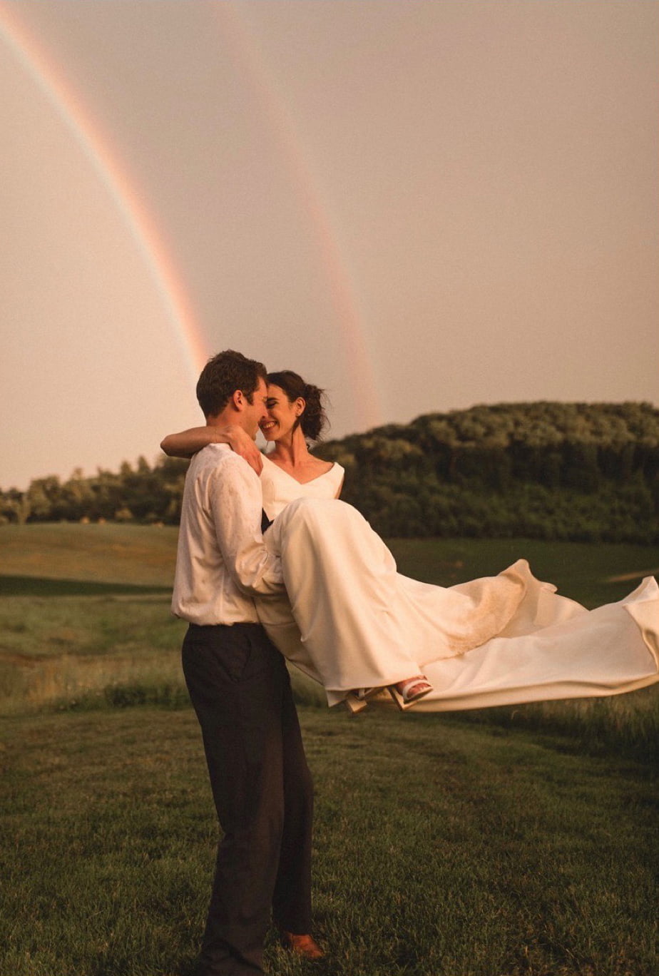 A country bride and groom hugging in front of a rainbow.