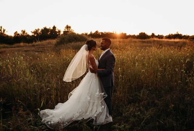 A bride and groom standing in a field at sunset.