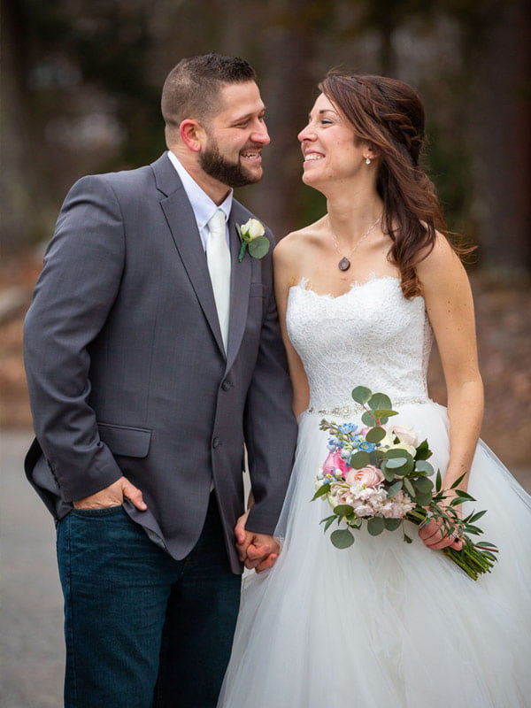 A country bride and groom smile as they walk down the road.