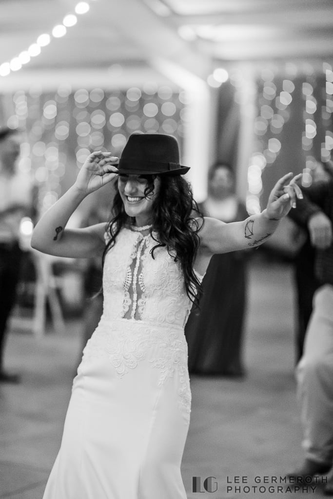 A bride wearing a hat dancing at a wedding.