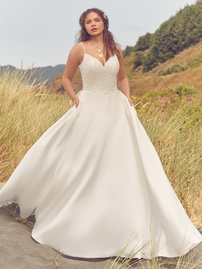 A woman in an Iona wedding dress standing on a beach.