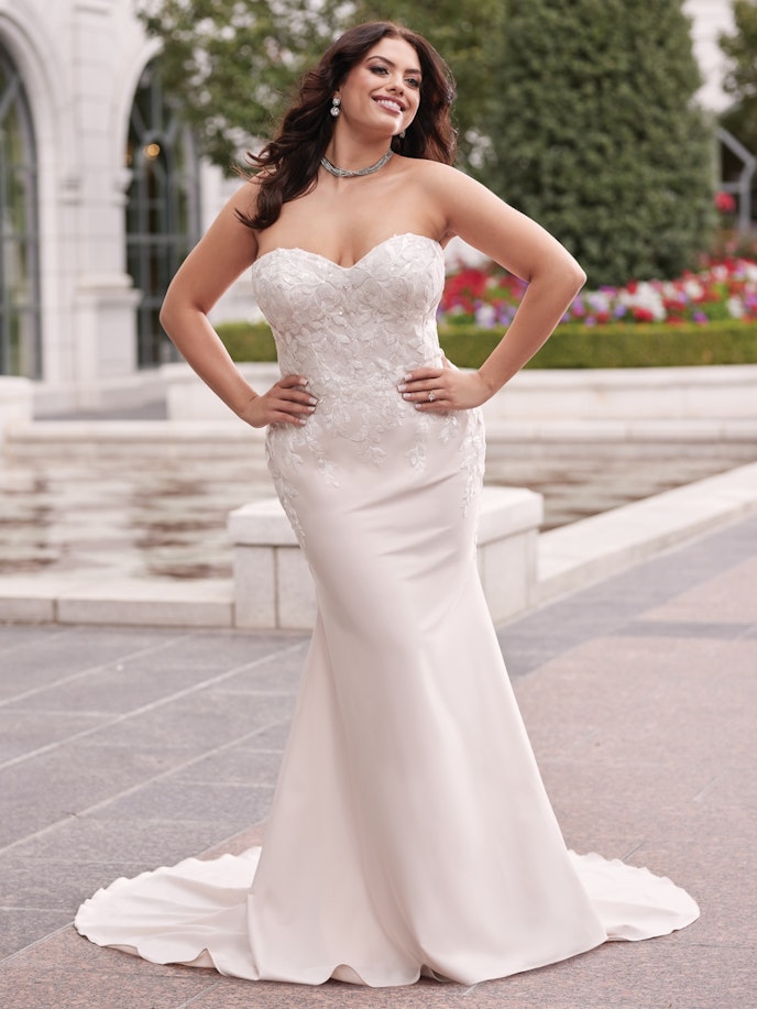 A plus size bride in a mermaid Lily wedding dress posing in front of a fountain.
