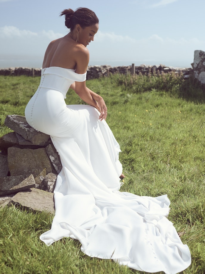 A woman in a Moriah wedding dress sitting on a rock.