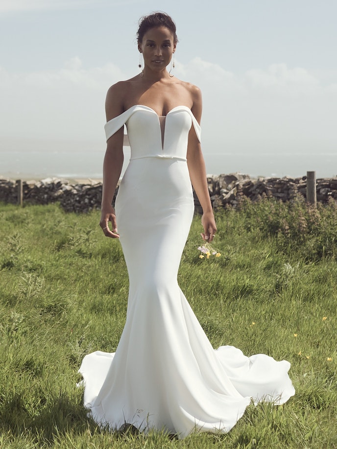 Moriah, wearing a white wedding dress, stands gracefully in a field.