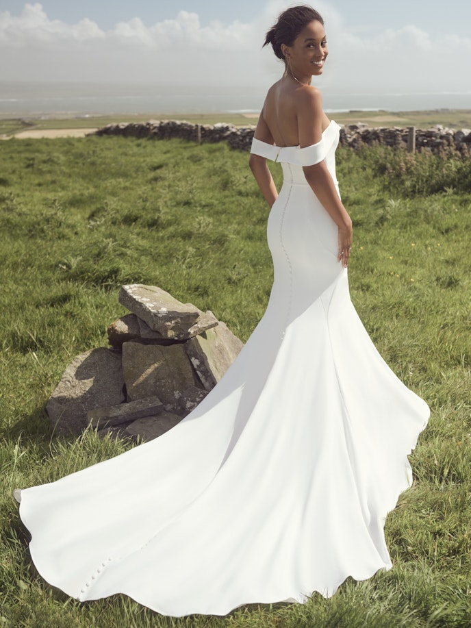 Moriah, wearing a white wedding dress, standing in a grassy field.