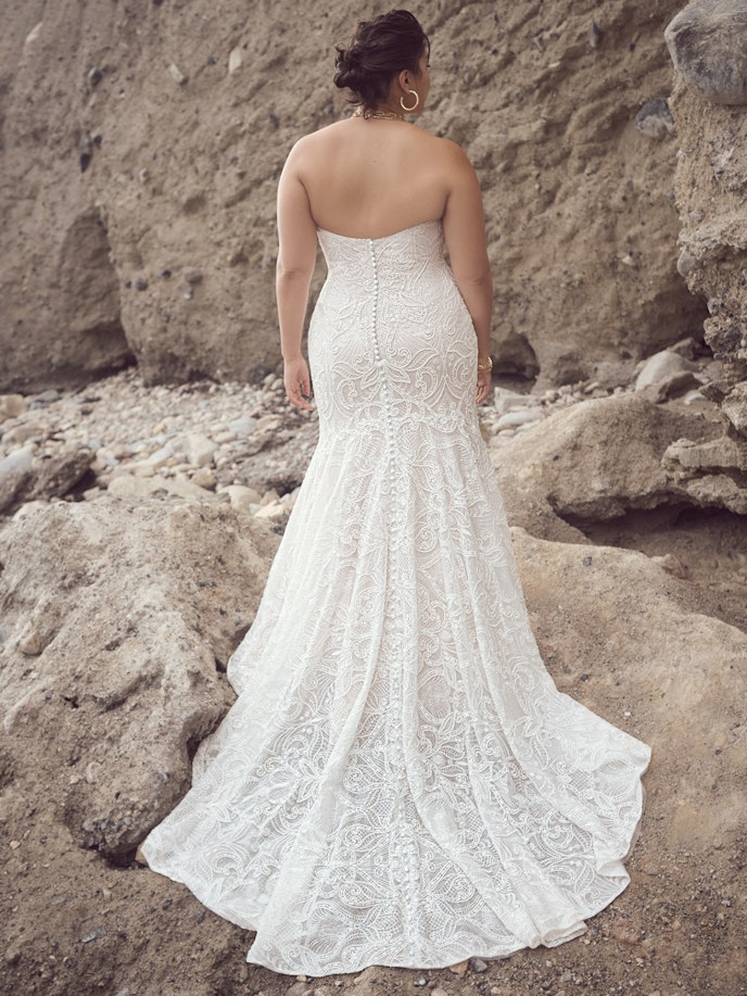 Juliette Wedding Dress - A woman gracefully stands on rocks, her back adorned in a captivating lace wedding dress.