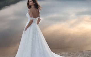 A bride, clad in a stunning white wedding dress, stands gracefully on the serene shore of a lake.