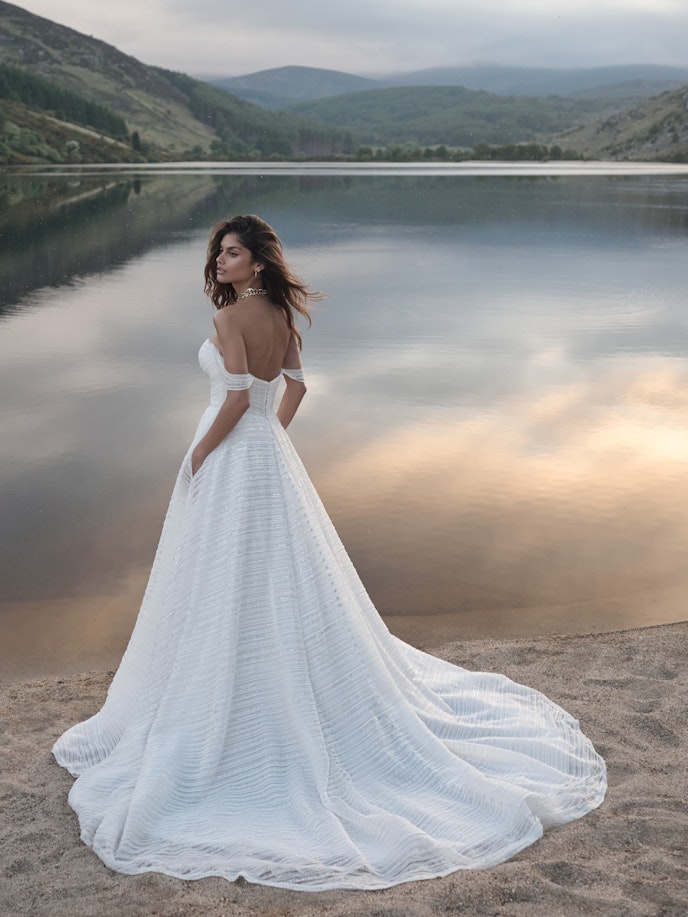 A bride, clad in a stunning white wedding dress, stands gracefully on the serene shore of a lake.