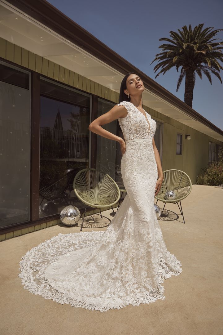 A woman in a lace wedding dress posing in front of a house.