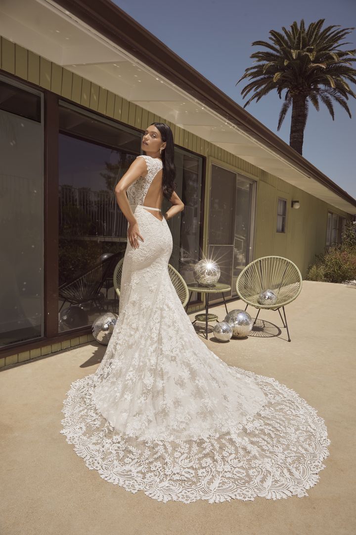 A woman in a lace wedding dress posing in front of a house.