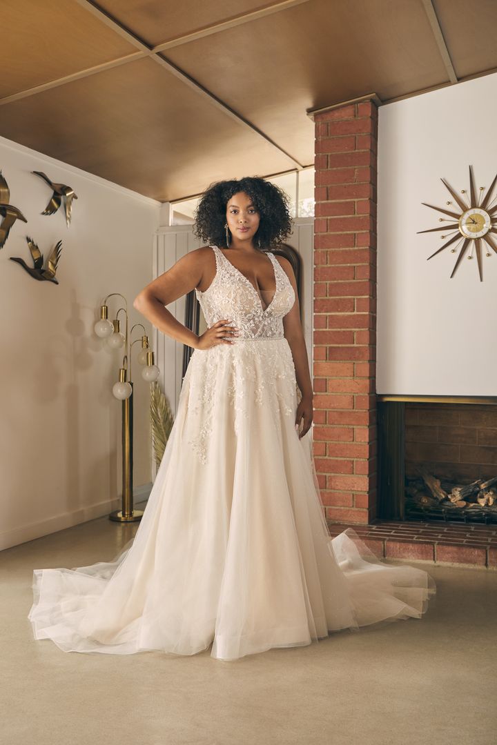A woman in a plus size wedding dress posing in front of a lilac fireplace.