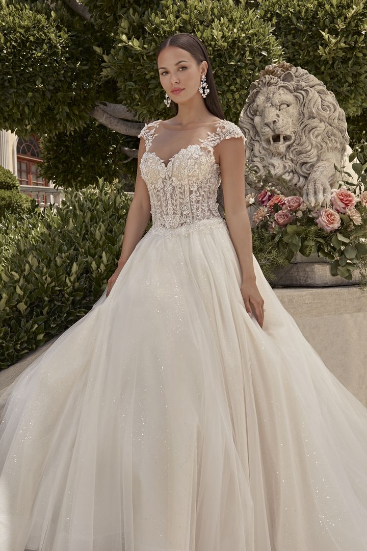 A woman in an elegant, embellished wedding gown stands beside a stone lion statue, surrounded by flowers.
